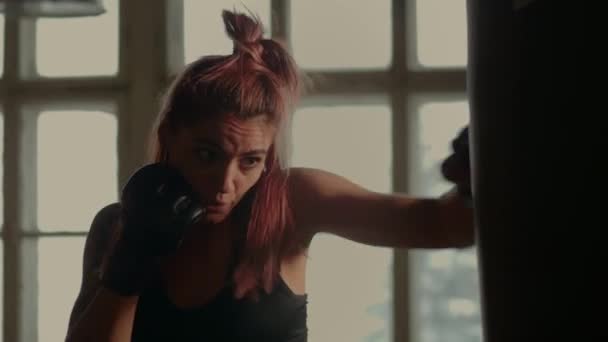 4k vídeo de atlético lutador feminino exercitando com saco de perfuração no ginásio durante o kickboxing e auto-defesa treino — Vídeo de Stock