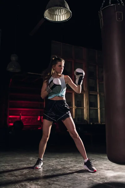 cool female fighter in boxing gloves trains in the gym. Mixed martial arts