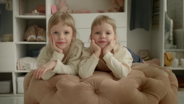 वॉर्डर पार्श्वभूमीवर ड्रेसिंग रूममध्ये एकत्र पॅड स्टूलवर हसू दोन स्टाइलिश लहान जुळी बहिणी मुलींचा 4K व्हिडिओ — स्टॉक व्हिडिओ