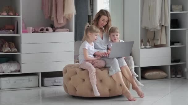 Молодая мать со своими дочерьми-близнецами выбирают вещи в своей уютной квартире онлайн — стоковое видео