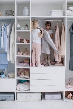 Aile gardırobu. Mutlu ikiz kardeşler dolapta doğal organik giysilerle rahat soyunma odasında neşeyle oynuyorlar.