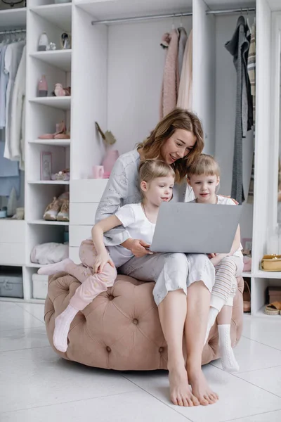 Mladá matka se svými dvojčaty dcery vybrat věci on-line ve svém útulném bytě Stock Fotografie