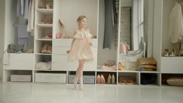 Gadis kecil yang menari menikmati gaun baru di ruang pakaian dengan latar belakang lemari pakaian dengan pakaian. Masa kecil, fashion dan gaya — Stok Video