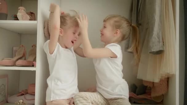 Семейный шкаф. Счастливые сестры-близнецы на полке в шкафу с натуральной органической одеждой в уютной гримерке играть радостно — стоковое видео