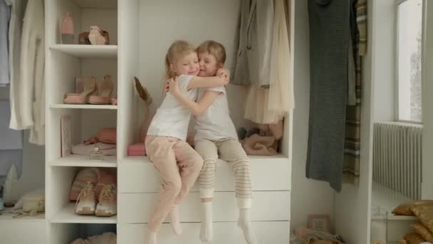Familjegarderob. Glada tvillingsystrar på hyllan i garderoben med naturliga ekologiska kläder i mysiga omklädningsrum leka glatt — Stockvideo