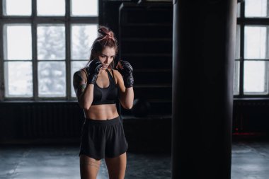 Spor salonunda kickboks ve savunma egzersizleri sırasında boks çantasıyla boks yapan atletik formda bir bayan boksör.