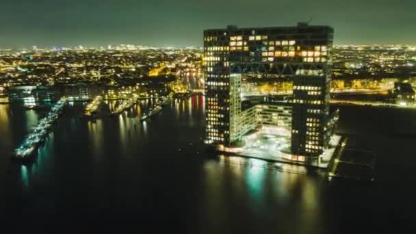 Amsterdam los Países Bajos, Vista aérea de un alto edificio de apartamentos en el centro de la ciudad hiperlapso por la noche con ferry llegando y saliendo — Vídeos de Stock