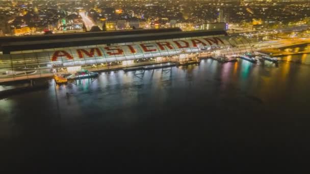 Hiperlapso de la vista aérea de la estación central de Ámsterdam Los transbordadores de los Países Bajos vuelan sobre aviones no tripulados disparados por la noche y el horizonte de la torre — Vídeo de stock