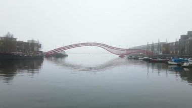 Amsterdam 'daki Phytonbrug veya Hoge Brug sisli bir kış günü kırmızı sanat mimarisinin altında uçuyor.