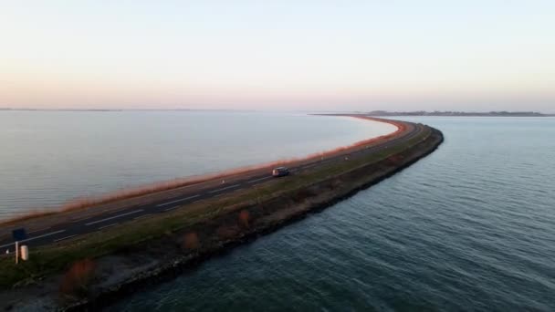 Small van on an open road with water surrounding driving at sunset. The Netherlands near Marken. — Stock Video