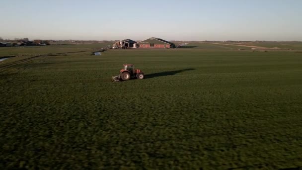 Tractor op een boerderij op een grasland bij zonsondergang filmische beelden van drone vanuit de lucht. — Stockvideo