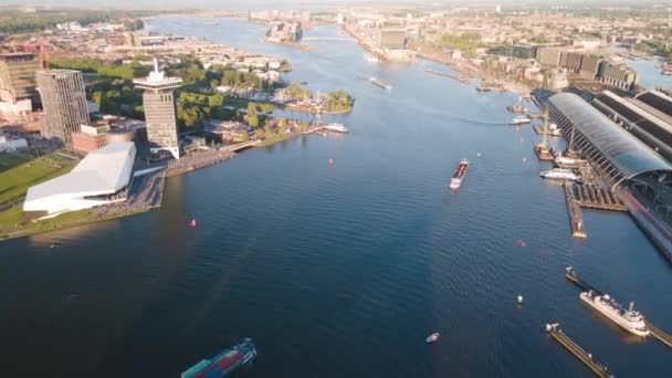 Luftaufnahme des Amsterdamer Hauptbahnhofs und Fähren, die den Fluss Ij bei Sonnenuntergang überqueren. Die Niederlande, Europa. — Stockvideo