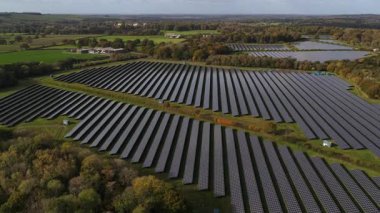 Aerial drone video capturing an expansive solar panel array or farm in the sunny countryside of Kent, United Kingdom. This image represents sustainable energy, clean power generation, and investment in future green technology.