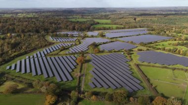 Aerial drone video capturing an expansive solar panel array or farm in the sunny countryside of Kent, United Kingdom. This image represents sustainable energy, clean power generation, and investment in future green technology.