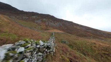 Cinematic FPV drone footage flying low along an ancient dry stone wall nestled in a beautiful, rugged mountain scene within a Wales National Park. This historic stone boundary is a classic feature of the UKs high-country landscape.