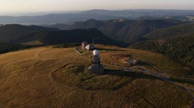 Alman Kara Ormanı 'ndaki Feldberg' in tepesindeki önde gelen telekomünikasyon ve hava durumu kulelerinin altın gün batımı hava aracı görüntüleri. Video modern altyapıyı ve doğayla olan bağlantısını vurguluyor..