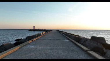 Hollanda 'daki IJmuiden limanının girişindeki Kuzey İskelesi' nin insansız hava aracı videosu. Gözetleme kulesi fenerini yakalıyor, gemileri geçiyor ve Kuzey Denizi üzerinde dramatik gün batımı manzarası var..