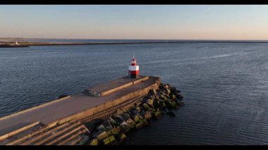 Hollanda 'daki IJmuiden limanının girişindeki Kuzey İskelesi' nin insansız hava aracı videosu. Gözetleme kulesi fenerini yakalıyor, gemileri geçiyor ve Kuzey Denizi üzerinde dramatik gün batımı manzarası var..