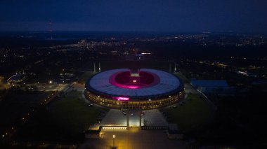 Geceleri Berlin Olimpiyat Stadyumu 'nun hava aracı görüntüsü mimariyi ve tarihi spor salonunu aydınlatıyor. Alman mirası, şehir manzarası ve dramatik gece şehir atmosferi sergileniyor..