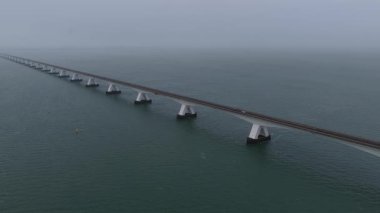 Zeeland Köprüsü 'nün Oosterschelde boyunca uzanan hava aracı videosu, Hollanda' daki ikonik Hollanda mühendisliği, su altyapısı ve atmosferik kıyı manzarasını gösteren, sonsuz bir sis bulutunun içinde beliriyor..