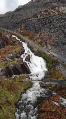 Kuzey Galler 'deki Tanygrisiau yakınlarında eski bir taş ocağı olan Llyn Cwmorthin' den akan bir şelalenin dikey hava görüntüsü engebeli dağlar ve tarihi sanayi manzaralarıyla çevrili..