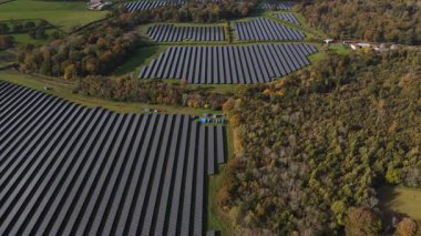 İngiltere 'nin kırsal kesimlerinde yenilenebilir enerji üretimi, fotovoltaik teknoloji ve sürdürülebilir elektrik üretiminin vurgulandığı güz günışığında İngiltere' nin kırsal kesimlerine kurulmuş güneş panellerinin insansız hava aracı görüntüleri.