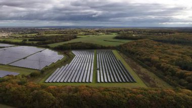 Kırsal alandaki güneş panelleri temiz, yeşil, yenilenebilir enerji üretiyor, bulutlu gökyüzünü yansıtan ve sonbahar ormanı ile çevrili gelecek için önemli bir sürdürülebilir kaynak.