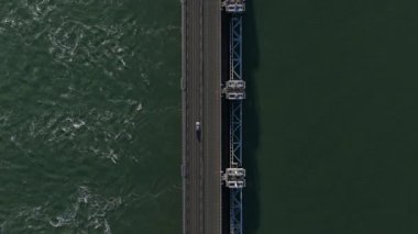 Yüksek açılı hava perspektifi, geniş ve modern bir köprüden geçen arabalar ve araçlarla sürekli bir trafik akışının olduğunu ve her iki tarafında zıt akımlarla derin yeşil suyun üzerinden geçtiğini gösteriyor.