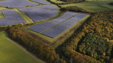 Sayısız fotovoltaik panelin gelecek için temiz ve sürdürülebilir elektrik üretmek amacıyla güneş ışığını yakaladığı geniş bir güneş çiftliğinin yüksek irtifa perspektifi.