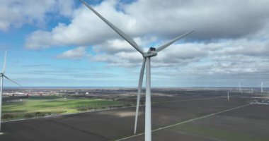 Rüzgâr türbininin dönen bıçaklarıyla hava görüntüsünü kapatın, kırsal alanda temiz ve sürdürülebilir enerji üretin, arka planda bir rüzgar çiftliği ve bulutlu mavi bir gökyüzü olsun.