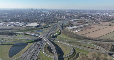 Çoklu üstgeçit ve rampadan oluşan karmaşık bir otoyol kavşağının havadan perspektifi, sisli mesafede geniş bir şehir silueti ile sürekli trafik akışını gösteriyor.