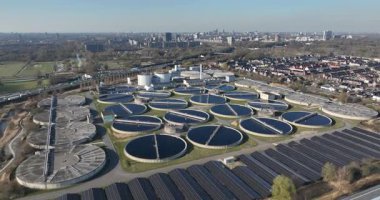 Dairesel tortu tankları ve çatı güneş panelleri olan modern bir kanalizasyon arıtma tesisinin geniş hava manzarası, yakındaki bir şehir için sürdürülebilir su arıtması gösteriyor.