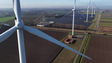 Havadan bakıldığında, büyük bir rüzgar türbini pervanesi üzerinde yoğunlaşıyor. Rüzgâr pervaneleri dönüyor. Daha geniş bir rüzgar tarlasının bir parçası, kırsal alanda güneş paneli kurulumuyla birlikte temiz ve yenilenebilir enerji üretiyor.