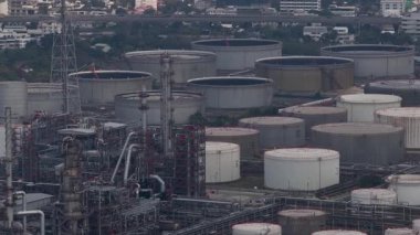 Birçok ham petrol depolama tankı, damıtma kuleleri ve boru hatları olan büyük bir petrokimyasal rafineri kompleksinin havadan görünüşü, yoğun bir şehir yakınında otoyol trafiği ile çalışıyor.