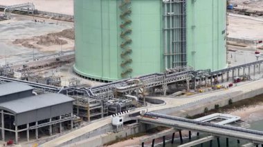 Bir sahil rafinerisindeki büyük bir sıvılaştırılmış doğalgaz depolama tankının sanayi manzarası, enerji işleme için geniş bir boru ve altyapı ağını gözler önüne seriyor.