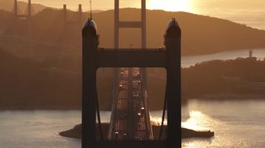 Hong Kong 'daki Ma Köprüsü' nün silueti. Muhteşem altın bir gün batımı sırasında parıldayan denizin üzerinden geçen araba trafiği güzel ve huzurlu bir manzara yaratıyor.