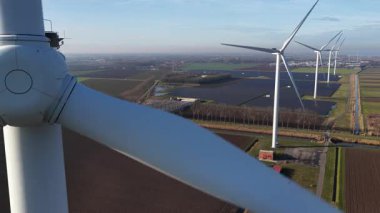 Açık ve güneşli bir günde kırsal alanda görülebilen bir dizi türbin ve güneş paneli çiftliğiyle birlikte dönen bir rüzgar türbininin büyük perspektifini kapat
