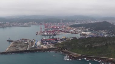 Keelung City, Tayvan 'ın sanayi limanına bakan, konteynır gemilerini, Gantry vinçlerini ve bulutlu, bulutlu bir gökyüzünün altındaki kentsel manzarayı gösteren