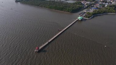 Yüksek açılı insansız hava aracı görüntüleri, bereketli bir mangrov ormanı olan kıyı köyünden engin, sakin denize uzanan, sakin ve pitoresk bir deniz manzarası gösteren uzun bir iskeleyi yakalıyor.