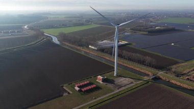 Rüzgâr çiftliği ve güneş panellerinin temiz, yenilenebilir enerji üreten yüksek açılı hava görüntüsü, pitoresk, düz bir tarımsal kırsal alanda konumlanmış sürdürülebilir bir enerji kaynağı gösteriyor.
