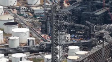 High aerial view of an expansive petrochemical complex with white storage tanks, dense pipework and construction activity highlighting large scale oil and gas processing infrastructure