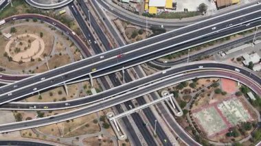 Yüksek irtifa aşağı perspektif araçların çok katmanlı bir otoyol kavşağında ilerlediğini gösteriyor, modern kentsel ulaşım altyapısı ve inşaat mühendisliğinin karmaşıklığını gösteriyor
