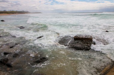 Köpüklü dalgalar bulutlu koşullarda kayalara çarpıyor.
