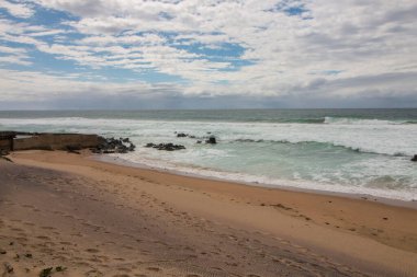 Dalgalar bulutlu bir günde sahildeki kayalara vuruyor.