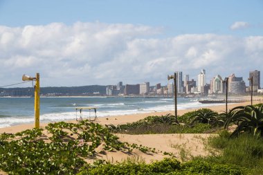 Arka planda bitki örtüsü ve binalarla kaplı bir kum tepesi