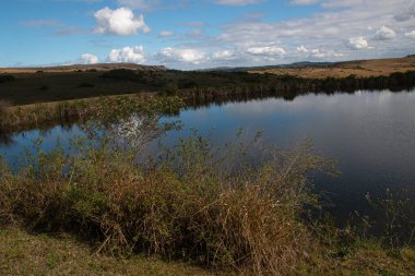 Bulutlar ve mavi gökyüzü kırsal göletin yüzeyine yansıyor