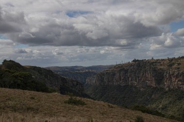Dik kayalıklar ağaçlık bir vadiye doğru iniyor.