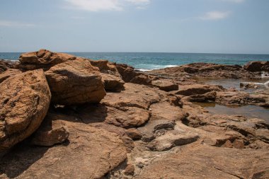 Kaya gölleri sahilde, ötesinde deniz var.
