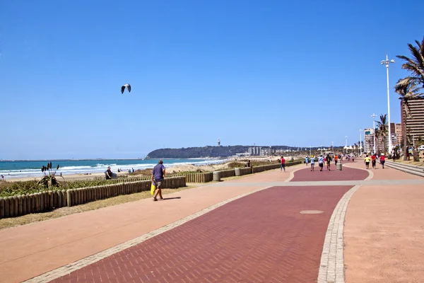 Persone che camminano lungo il lungomare lastricato sul fronte spiaggia — Foto Stock