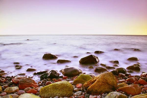 Mañana romántica en el mar. Grandes rocas que sobresalen del nivel del agua suave. Horozon rosa con los primeros rayos de sol caliente . — Foto de Stock